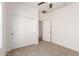 Carpeted bedroom with a ceiling fan and a closet with sliding doors, adjacent to the entryway to another room at 15674 W Mackenzie Dr, Goodyear, AZ 85395