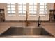 An undermount stainless steel sink features both gold and black faucets below a window with white shutters at 44236 W Adobe Cir, Maricopa, AZ 85139