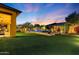 Well-maintained backyard with green lawn, pool, mature trees, and elegant outdoor lighting at dusk at 6918 E Ivyglen St, Mesa, AZ 85207
