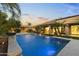 Outdoor pool area at twilight with lush landscaping, fire bowls, and a covered patio at 6918 E Ivyglen St, Mesa, AZ 85207