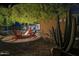 Inviting firepit area with red Adirondack chairs, desert landscaping and views of the home's interior at night at 8248 E Arroyo Hondo Rd, Scottsdale, AZ 85266