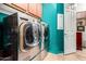 Laundry room with stainless steel front-load washer and dryer units and a teal accent wall at 20962 W Thomas Rd, Buckeye, AZ 85396