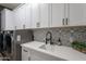 Contemporary laundry room featuring sleek white cabinetry, matte black hardware, and a mosaic tile backsplash at 27809 N Silverado Ranch Rd, Peoria, AZ 85383