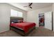 Bedroom with a red comforter on the bed, ceiling fan, carpet and ensuite bathroom at 3113 N 303Rd Dr, Buckeye, AZ 85396