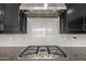 Close-up of a stainless steel gas cooktop and hood with a marble backsplash and dark cabinetry at 14177 W Calle Lejos --, Surprise, AZ 85387