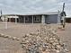 Charming single-story home with a covered carport, grey siding, and a decorative rock garden at 329 N 83Rd Pl, Mesa, AZ 85207
