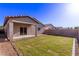 Landscaped backyard featuring green grass, covered patio, block fence, and sliding glass door at 45722 W Sky Ln, Maricopa, AZ 85139