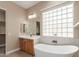 Bright bathroom featuring a soaking tub, glass block window, and wood vanity with white countertop at 6805 S Sapphire Way, Chandler, AZ 85249
