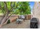 Backyard gravel patio area with small seating and barbeque under mature trees and privacy wall at 7673 N Via De Platina Dr, Scottsdale, AZ 85258