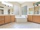 Bathroom featuring dual sinks, maple cabinets, mirrors, and a standalone soaking tub at 19803 N Desert Song Ct, Surprise, AZ 85374
