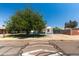 A well-maintained single-story home with a large shade tree in the front yard under a bright blue sky at 8132 W Pierson St, Phoenix, AZ 85033