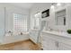 Bathroom features a bathtub with a glass enclosure and dual vanity sinks with white cabinets and wood flooring at 11993 E Mission Ln, Scottsdale, AZ 85259