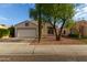 Single-story home with a two-car garage, desert landscaping, and a mature shade tree at 10735 W Bermuda Dr, Avondale, AZ 85392