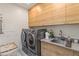 Laundry room with wood cabinets, modern washer and dryer set, and stainless steel sink at 2 Biltmore Est # 313, Phoenix, AZ 85016