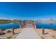 Scenic view of a private community wooden dock on a tranquil lake reflecting a blue sky with sparse trees at 38082 W Santa Barbara Ave, Maricopa, AZ 85138