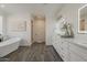 Bathroom featuring double sinks, white cabinets, lighted mirrors, a soaking tub and wood-look floors at 3834 E Clarendon Ave, Phoenix, AZ 85018