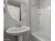 Bathroom with a single pedestal sink, round mirror and a bathtub with white tiles at 2028 N 77Th Ln, Phoenix, AZ 85035