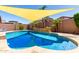 Backyard pool with a sunshade, rock waterfall feature, and lush landscaping at 13123 W Cottontail Ln, Peoria, AZ 85383