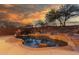 Backyard pool and spa with rock features are framed by lush landscaping and a vibrant sunset sky at 14056 E Desert Cove Ave, Scottsdale, AZ 85259