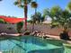 Lush backyard pool with a rock waterfall feature, mature palm trees, and a shade sail for sunny relaxation at 656 W Devon Ct, Gilbert, AZ 85233