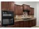 Close-up view of a kitchen featuring dark wood cabinets, stainless steel appliances, and a granite countertop with a tile backsplash at 4721 N Aldea W Rd, Litchfield Park, AZ 85340