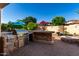 Inviting outdoor kitchen featuring a built-in grill, stone bar, and fire pit under a clear blue sky at 816 W Sycamore Ct, Litchfield Park, AZ 85340