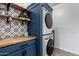 Convenient laundry room with modern stacked washer and dryer and a wooden countertop and shelving at 11829 W Patrick Ln, Sun City, AZ 85373