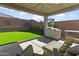 A covered back patio area with furniture overlooks the backyard with green turf at 7180 W Tombstone Trl, Peoria, AZ 85383