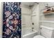 Tiled shower-tub combination next to a white toilet and shelving unit, highlighted by a floral shower curtain at 1402 E Guadalupe Rd # 114, Tempe, AZ 85283