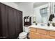 Well-lit bathroom featuring a vanity with a wood cabinet and a dark shower curtain at 14393 W Wethersfield Rd, Surprise, AZ 85379