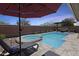 Lounge poolside under a red umbrella in this backyard oasis featuring a spa, seating area, and a brick privacy wall at 14393 W Wethersfield Rd, Surprise, AZ 85379