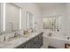Bright bathroom featuring dual sinks with gray cabinets, a soaking tub with glass block window, and white tile at 3406 E Pyrenees Pass, Phoenix, AZ 85018