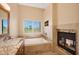 Spa-like bath with marble countertops, soaking tub, fireplace, and scenic views through window at 7272 E Gainey Ranch Rd # 23, Scottsdale, AZ 85258