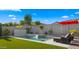 Beautiful backyard pool with a waterfall feature, artificial turf, and lounge chairs under a red umbrella at 13820 W Weaver Ct, Litchfield Park, AZ 85340