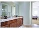 Bathroom with double sink vanity, wood cabinets, decorative mirror and access to the adjacent bedroom at 1707 E Carob Dr, Chandler, AZ 85286