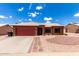 Charming single-story home featuring a red garage door, beautiful desert landscaping, and a white tiled roof at 6302 E Portia St, Mesa, AZ 85215