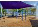 Swings hang beneath a vibrant purple canopy, offering a shady spot for fun in this community playground at 16186 W Port Royale Ln, Surprise, AZ 85379