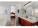 Bright bathroom featuring double sinks, wood cabinetry, and a view into the Primary bedroom at 9124 W Williams St, Tolleson, AZ 85353