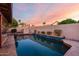 A backyard pool with a stone border is surrounded by a brick wall and lush landscaping under a beautiful sunset sky at 11085 E Mary Katherine Dr, Scottsdale, AZ 85259