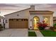 Inviting home exterior featuring a stucco facade, a two-car garage, and a charming arched entryway with vibrant red flowers at 20784 W Minnezona Ave, Buckeye, AZ 85396