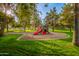Community playground featuring a red play structure surrounded by mature trees and lush green grass at 1825 W Ray Rd # 1070, Chandler, AZ 85224