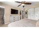 Cozy main bedroom features carpet flooring, a ceiling fan, a dresser, a large TV, and an en-suite bathroom at 1733 W Surrey Ave, Phoenix, AZ 85029