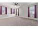 Bright bedroom with neutral carpet, ceiling fan, and three windows draped with purple curtains at 19022 W Shangri La Rd, Surprise, AZ 85388