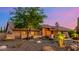 Single-story home with desert landscaping, rocks, and a mature shade tree at dusk at 5861 E Anderson Dr, Scottsdale, AZ 85254