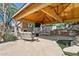 Covered outdoor living space with stone fireplace, outdoor kitchen, and seating area by a pond at 6428 W Eugie Ave, Glendale, AZ 85304