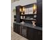 Modern bar area with a wine fridge, black cabinets, and decorative lighting and shelving at 7527 E Nestling Way, Scottsdale, AZ 85255