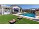 Resort-style backyard with pool, outdoor kitchen, lush landscaping, and lawn game area at 5218 N Tiller Dr, Litchfield Park, AZ 85340