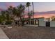 Inviting single-story home with desert landscaping, palm trees, and unique arched windows under a colorful dusk sky at 1736 N Ashbrook Cir, Mesa, AZ 85213