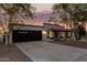 Attractive home exterior showcasing a dark garage door, desert landscape, and a charming arched entrance at twilight at 1736 N Ashbrook Cir, Mesa, AZ 85213
