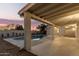 Covered patio offering a shaded retreat with views of the sparkling pool and lush landscaping at dusk at 1736 N Ashbrook Cir, Mesa, AZ 85213